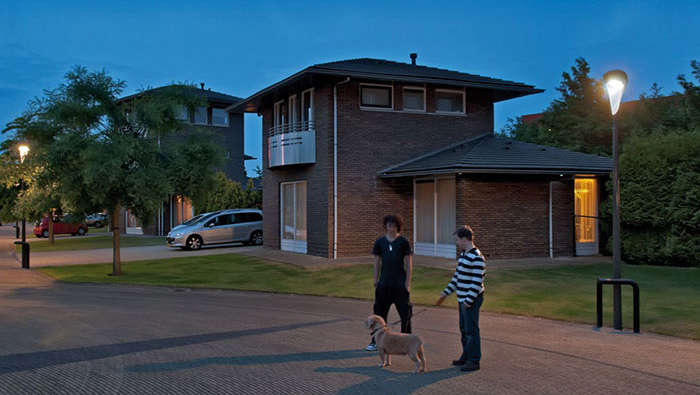 Two people are walking with their dog in the street under Philips city lighting  