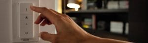 "Hand adjusting Philips smart LED dimmer switch, controlling ambient lighting in cozy living room with bookshelves."