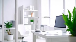 A bright white room shows a desk with a computer and a table lamp on it