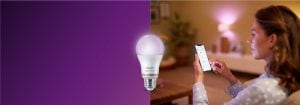 "Woman controlling smart LED lighting via smartphone app, creating warm ambiance in cozy living room with connected home technology."